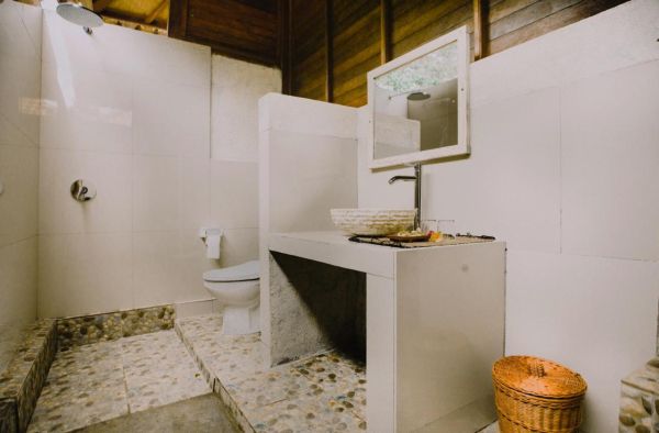 Rustic tropical bathroom with wooden walls, pebble tile floor, woven sink basin, and open shower. - Bali Villas